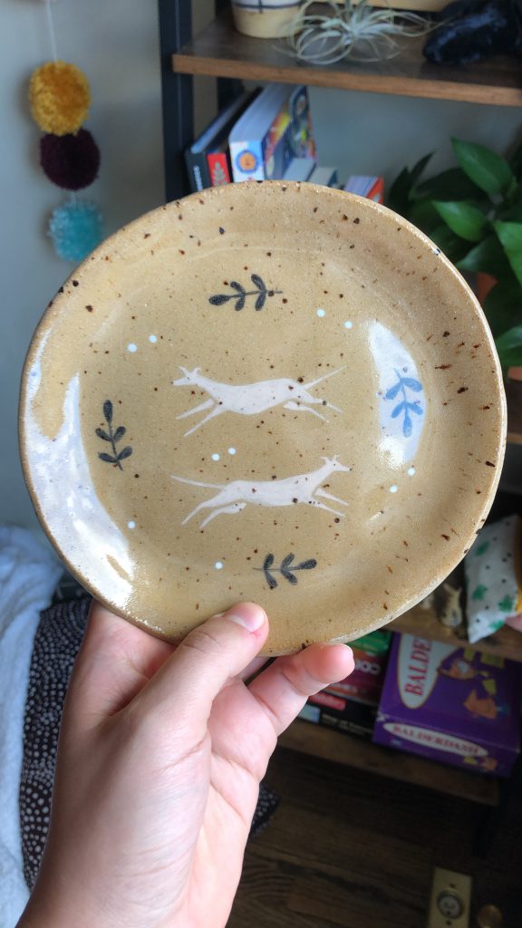 A handmade ceramic plate with a greyhound and leaves illustration glazed onto it