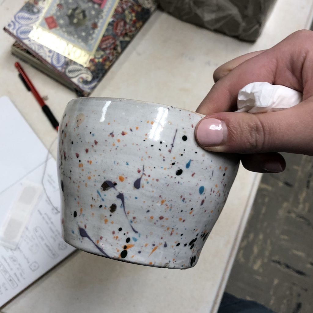 A hand holds a ceramic pot with a splatter glaze effect