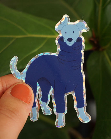 A hand holds a italian greyhound sticker in front of some greenery