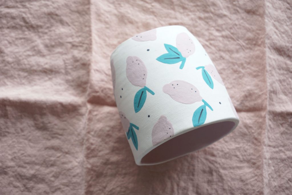 A ceramic mug with alemon pattern rests on its side atop a pink linen napkin