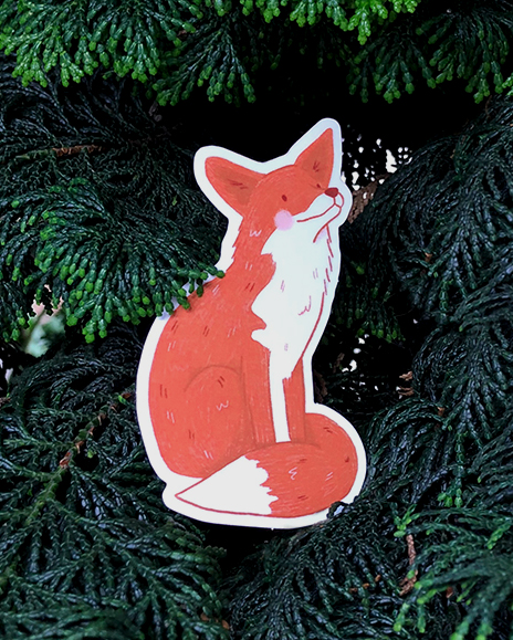 A fox sticker rests on some evergeen branches