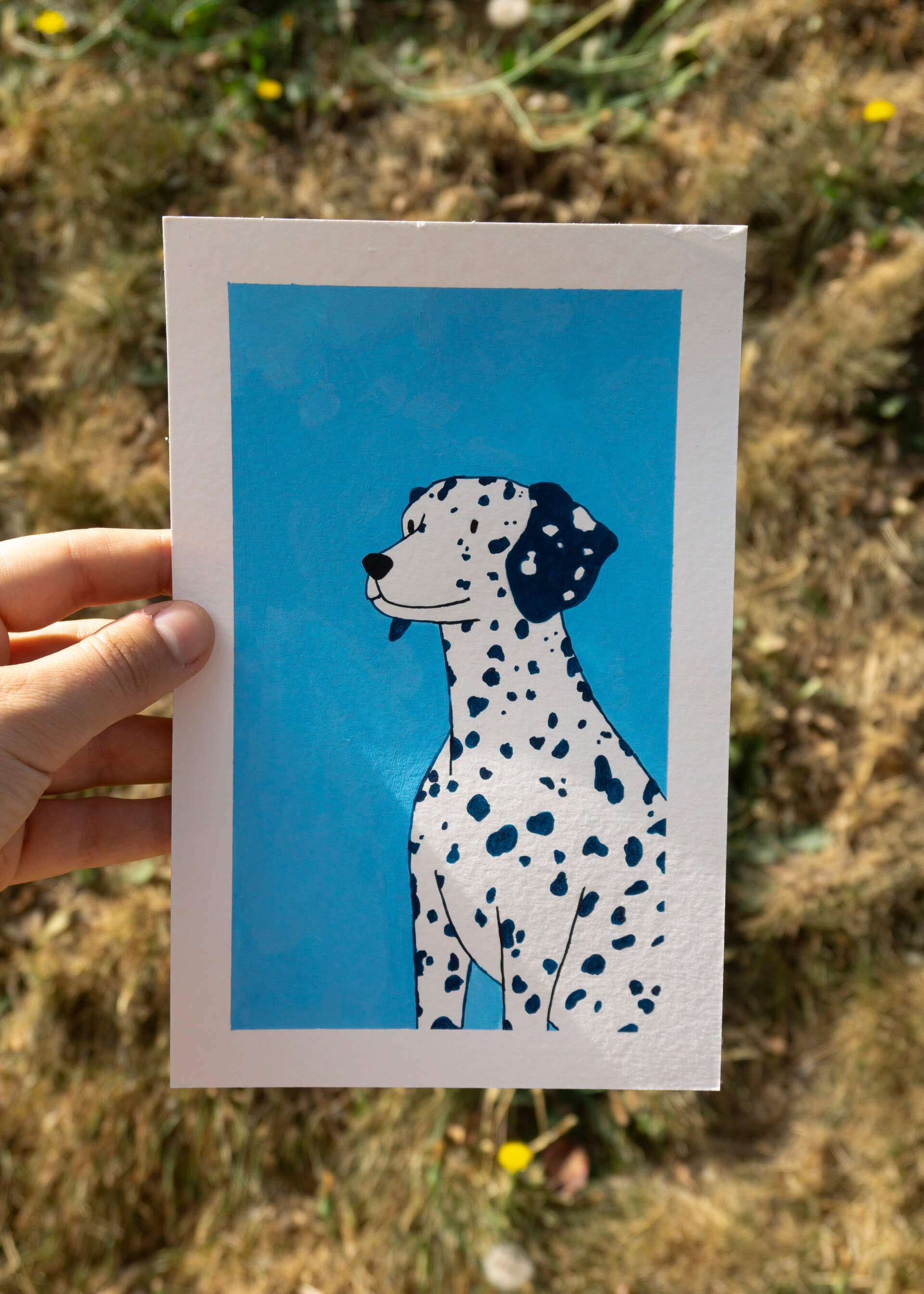 A hand holds up a gouache painting of a dalmatian on a blue background