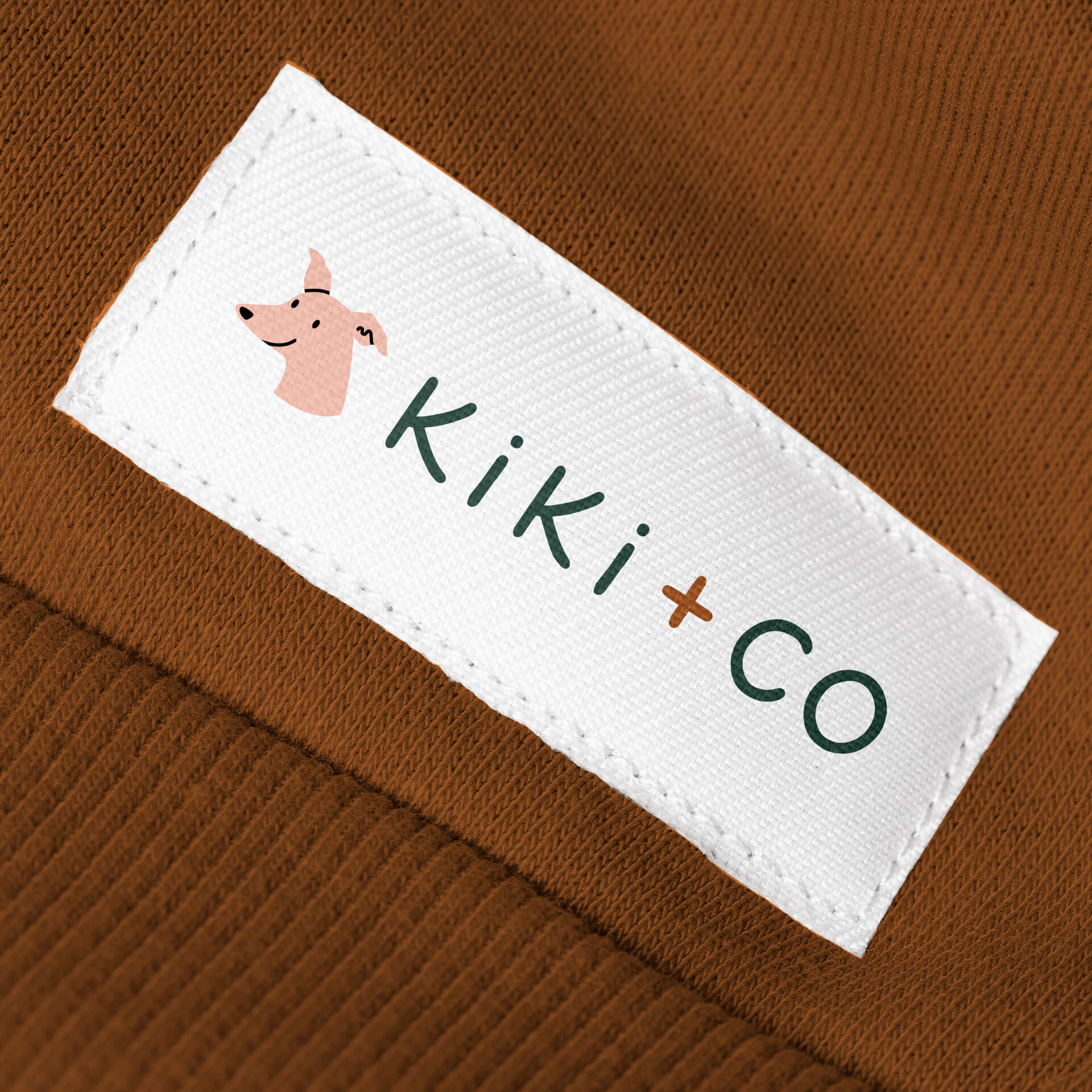 A white clothing label featuring the kiki & co logo on a dark orange garment